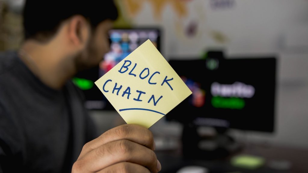 an employee of a cannabis and cryptocurrency company, holding up a sticky note that reads "Block Chain"